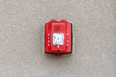 Red fire alarm siren with flashing light strobe isolated on gray cement wall outdoor. Fire safety. clipart
