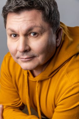 Yakışıklı, iyimser, orta yaşlı bir adamın, kameraya bakıp olumlu duygularını ifade eden kentsel kapüşonlu kapüşonlu bir giysisi olan portresi. Gri arka planda izole edilmiş kapalı stüdyo görüntüleri.