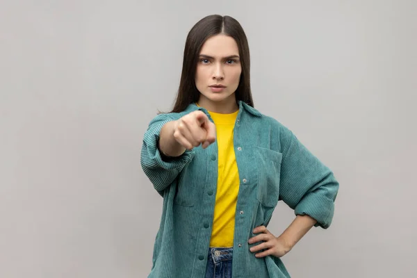 Hey you. Portrait of angry bossy woman pointing finger to camera, looking with suspicion and accusing, choosing guilty, wearing casual style jacket. Indoor studio shot isolated on gray background.