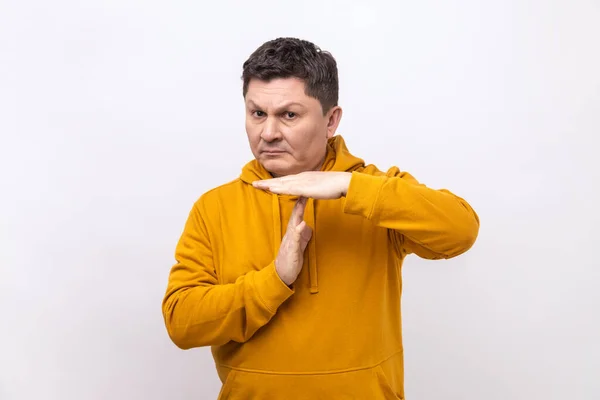 I need more time. Portrait of frustrated man showing time out gesture, looking at camera, hurry to meet deadline, wearing urban style hoodie. Indoor studio shot isolated on white background.