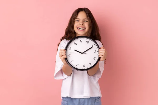 笑顔の肖像画喜びの少女白いTシャツを着て壁の時計を保持し 完成したホームタスクに満足し 締め切り 満足している ピンクの背景に隔離された屋内スタジオショット — ストック写真