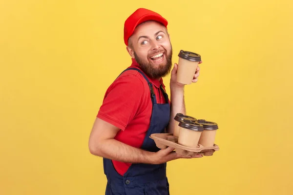 Kahveyi Götüren Mavi Tulumlu Kırmızı Şapkalı Komik Teslimatçının Yan Görünüm — Stok fotoğraf