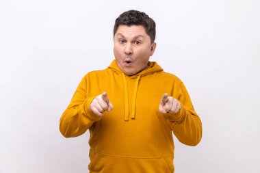 Şaşkın adamın portresi kamerayı işaret ediyor ve şaşkın bir ifadeyle bakıyor, bir şeye çok şaşırmış, şehir tarzı kapüşonlu bir şey giyiyor. Beyaz arka planda izole edilmiş kapalı stüdyo görüntüleri.