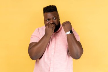 Pembe gömlek giyen, akıllı saatini gösteren ve tırnaklarını yiyen sinirli sakallı bir adamın portresi için yeterli zaman yok. Sarı arka planda kapalı stüdyo çekimleri.