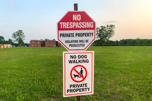 The prohibitive sign on the label No trespassing, private property, violators will be prosecuted, no dog walking against the green lawn in sunlight.