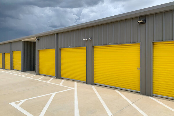 Storage unit buildings site outside, owners property. Road with markings leading to garages with yellow roller doors.