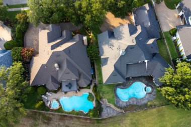 Yazın yeşil çimenler ve ağaçlarla çevrili yüzme havuzları olan lüks konakların insansız hava aracı görüntüsü.