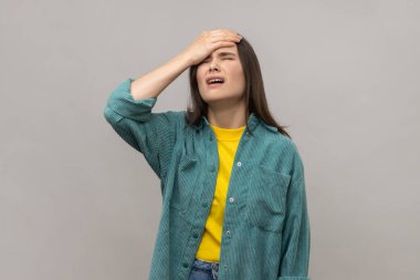 facepalm jesti olan şanssız bir kadın, pişmanlık ve keder hisseden, hata için kendini suçlayan, yenilgi yüzünden hayal kırıklığına uğrayan, günlük tarz ceket giyen. Gri arka planda izole edilmiş kapalı stüdyo görüntüleri.