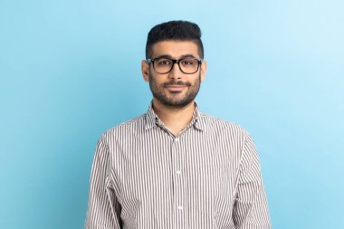 Optik gözlüklü, gülümseyen mutlu iş adamının portresi gülümseyerek kameraya bakıyor, çizgili gömlek giyiyor. Mavi arka planda kapalı stüdyo çekimi.