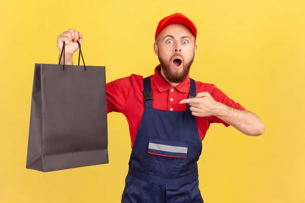 Lenyűgöző Izgatott Futár Kék Egyenruhában Fekete Bevásárló Táskára Mutatva Megrendelést — Stock Fotó