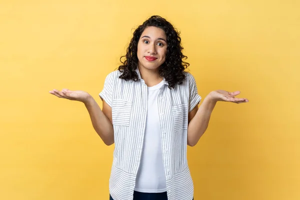 I am not sure. Portrait of ambiguous woman with dark wavy hair standing with raised arms, looking away and don\'t know what to do. Indoor studio shot isolated on yellow background.