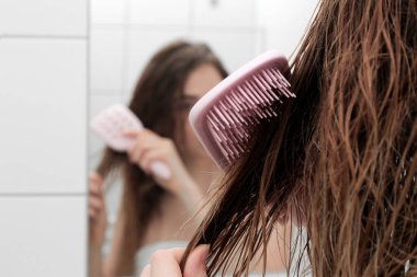 young beautiful girl in the bathroom with wet hair with a comb. in a white bath. hair care and health