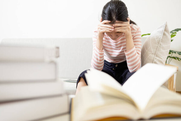 Anxious teenage girl has tension during exam preparation,Stressed worried asian student while studying reading a textbook before final test at her home,afraid of failing the exam,education concept