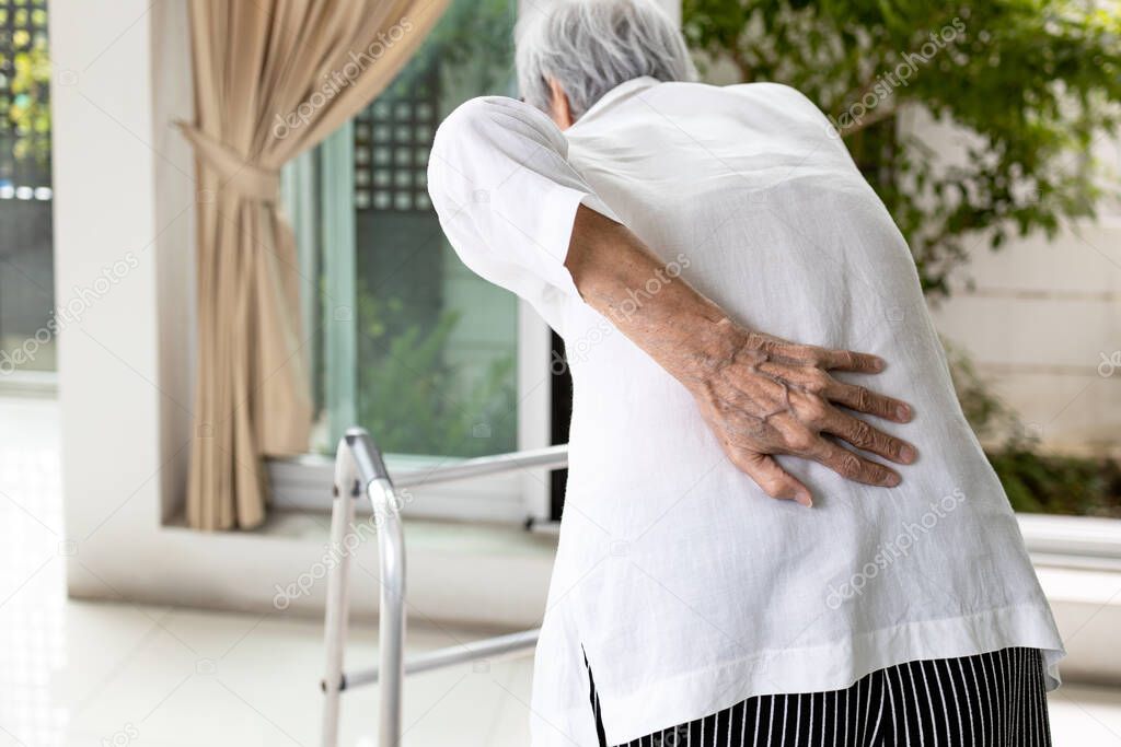 Hand of asian old elderly touch lower back muscles,senior patient with walker stick,suffering from back pain,backache from spinal joint problems,myositis,painful of lumbago,health care,medical concept