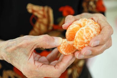 Portakal meyvesi yakın, elinde sulu portakal tutan yaşlı kadın, soyulmuş taze mandalina gösteren yaşlı kadın, mandalinadan C vitamini, lezzetli ve iştah açıcı, sağlıklı yiyecek, sağlık konsepti.