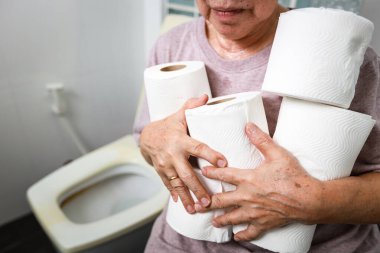 Senior woman carrying holding a lot of toilet paper in bathroom,many rolls of toilet paper for wiping,cleaning after urination or defecation,frequent urination problems or diarrhea in the old elderly clipart