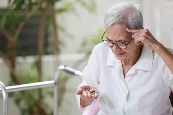 Asian senior patient with Alzheimer\'s disease or dementia,look at the pills capsules on her palm,trying to think,confused,old elderly people forget to take the medication,fail to remember or amnesia