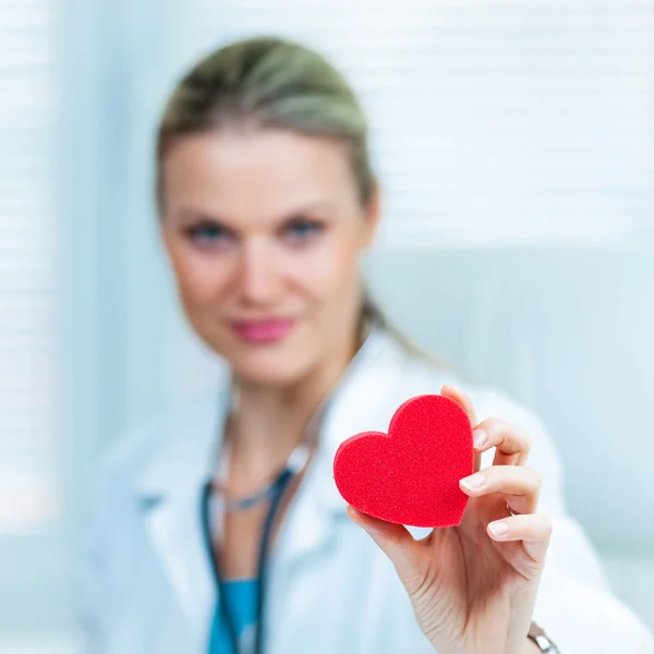 Αρκετά νεαρή γυναίκα γιατρό δείχνει μια κόκκινη καρδιά σε ασθενοφόρο (ρηχά βάθος πεδίου, να χρώμα εικόνα τονισμένο) Εικόνα Αρχείου