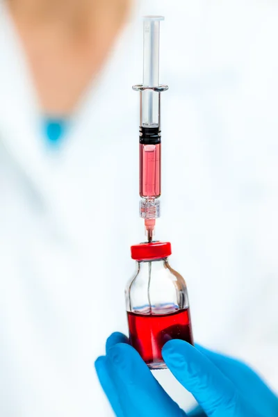 Ученый держит красную медицинскую жидкость в ампуле и инъекции — стоковое фото
