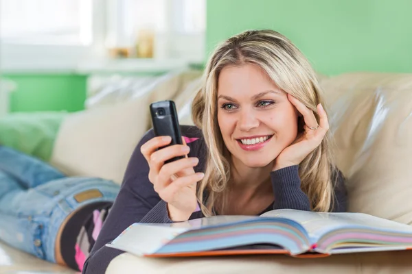 Young Woman Sending SMS with Mobile Phone While Lying at Home on — Stock Photo, Image
