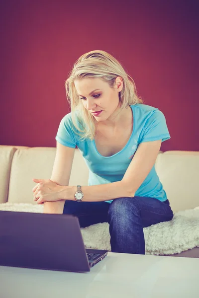 Pretty Young Girl está sentada en casa y usando su computadora portátil (color — Foto de Stock