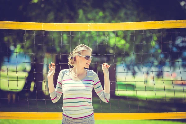 Hermosa mujer se apoya en la red de voleibol de playa durante un Imagen De Stock