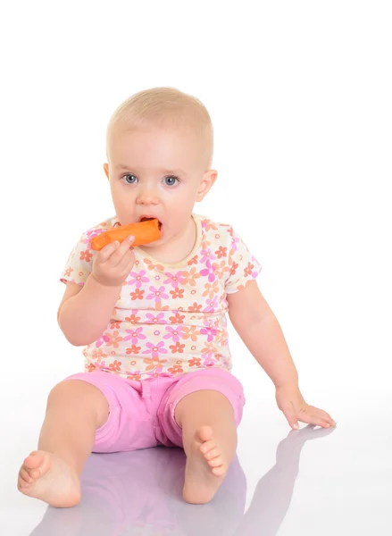 Süßes kleines Baby isst eine Möhre auf dem Boden sitzend auf weiß Stockfoto