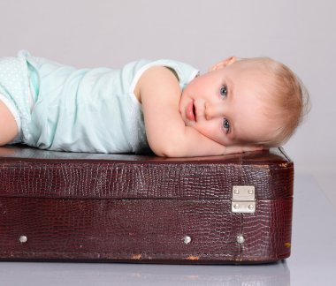 Baby girl playing with suitcase on grey background