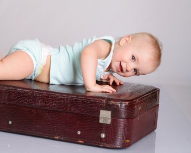 Baby girl playing with suitcase on grey background