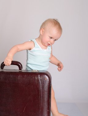Baby girl playing with suitcase on grey background