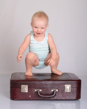 Baby girl playing with suitcase on grey background