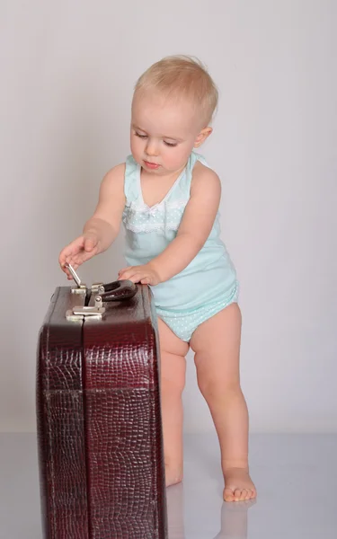 Dziecko dziewczynka gra z walizką na szarym tle — Zdjęcie stockowe