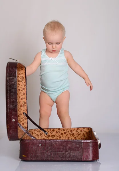 Bambina che gioca con la valigia su sfondo grigio — Foto Stock