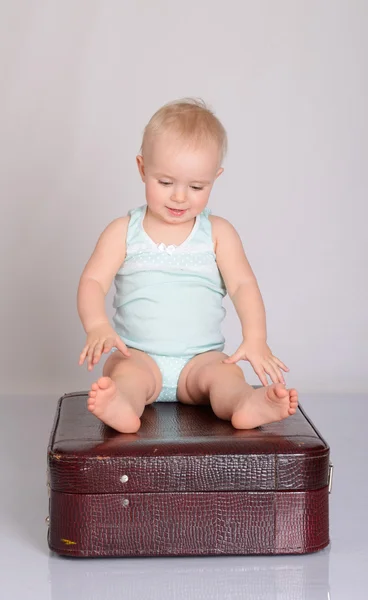 Baby girl playing with suitcase on grey background — Stock Photo, Image