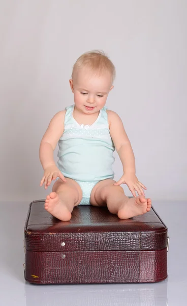 Baby girl playing with suitcase on grey background