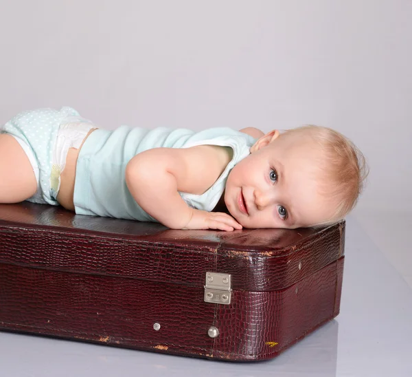 Bambina che gioca con la valigia su sfondo grigio — Foto Stock