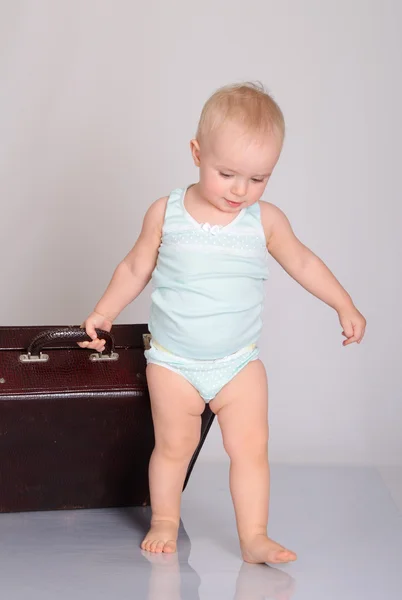Baby flicka som leker med resväska på grå bakgrund — Stockfoto