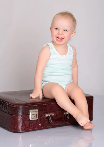 Baby girl playing with suitcase on grey background