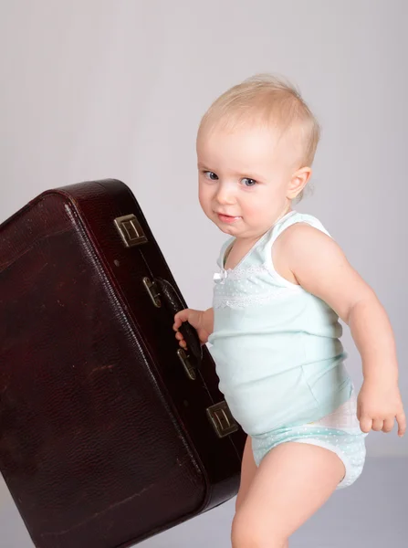 Baby girl playing with suitcase on grey background