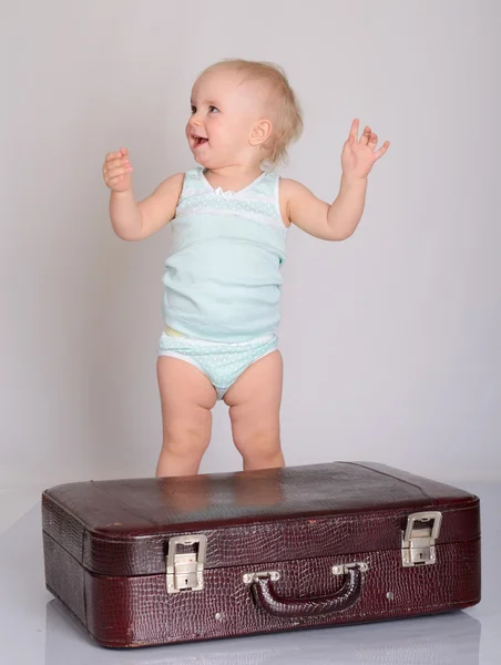 Niña jugando con la maleta sobre fondo gris — Foto de Stock