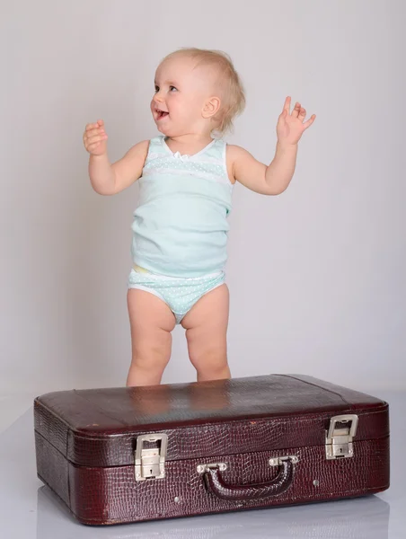 Baby girl playing with suitcase on grey background