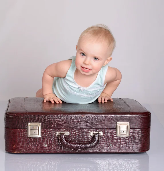 Dziecko dziewczynka gra z walizką na szarym tle — Zdjęcie stockowe