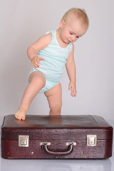 Mädchen spielt mit Koffer auf grauem Hintergrund — Stockfoto