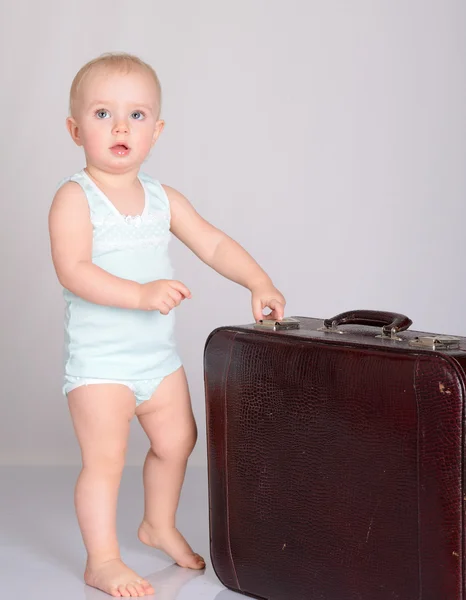 Baby flicka som leker med resväska på grå bakgrund — Stockfoto
