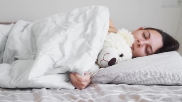 Genç bir kadın yatak odasında oyuncak ayıyla uyuyor. Telefon bağımlılığı, uykusuzluk. Sosyal medyayı kontrol ediyorum. Circadian rhuthm. — Stok video