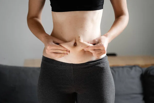 Ung kvinna hemma håller magen fet med händerna. Begreppet kroppsneutralitet. Accepterar kroppen och vikten. Ohälsosamt kolhydratintag. — Stockfoto
