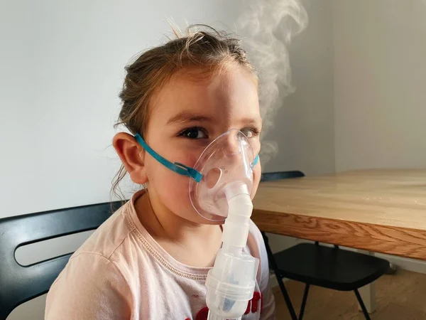 Enfermo adorable niña preescolar con máscara de nebulizador en casa. Tratamiento de la bronquitis con nebulosa inhalatoria. — Foto de Stock