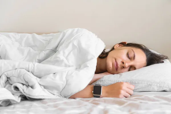 La joven se duerme. Adicción al teléfono, insomnio. Intenta dormirte. Seguimiento del sueño en el teléfono y reloj inteligente. Ritmo circadiano. — Foto de Stock