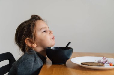 Mutsuz kız çocuğu siyah kaseden soğanlı ekmek yiyor. Mutfaktaki çocuğun yemek yerken çekilmiş hayat fotoğrafı, Çığlık atan çocuk. Seçici yiyici