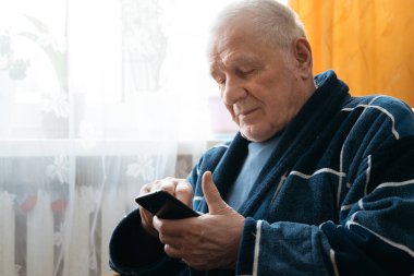 Akıllı telefonlu yaşlı bir adam koltukta oturuyor ve sosyal medyada kayıyor.. 